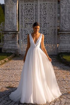 a woman in a white wedding dress standing on a cobblestone walkway with an ornate gate behind her