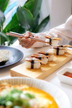 a person holding chopsticks over sushi on a wooden board next to other plates