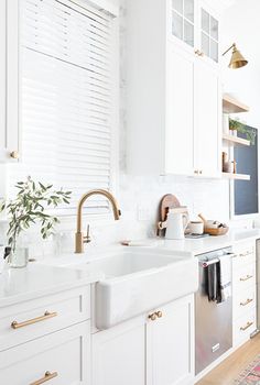 a kitchen with white cabinets and gold faucets, an area rug on the floor