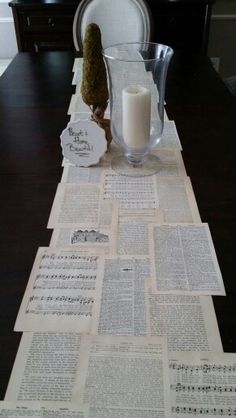 a table topped with lots of paper next to a vase filled with a white candle