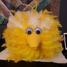 a yellow stuffed animal with big eyes and feathers on it's head sitting on a table