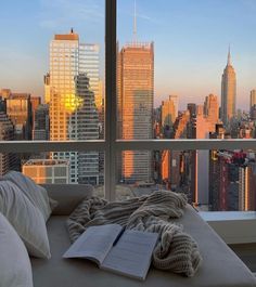 an open book is sitting on a couch in front of a window overlooking the city