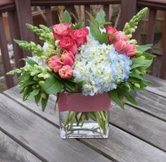 a vase filled with pink and blue flowers on top of a wooden table next to a fence