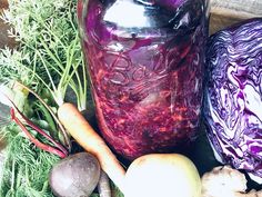 a jar filled with purple liquid surrounded by vegetables