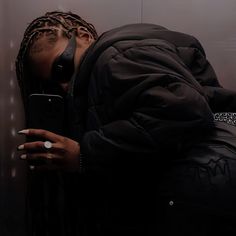 a person with dreadlocks leaning against a wall holding a cell phone to their face