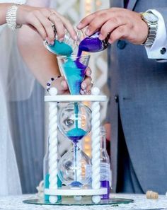 a man and woman are making an hourglass with blue liquid in it on top of a table