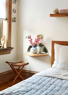 a bed sitting next to a window with flowers in vases on top of it