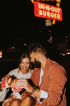 a man and woman sitting next to each other in front of a neon sign at night