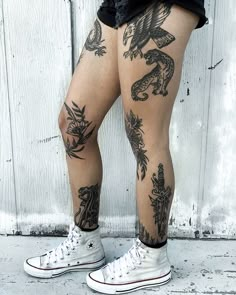 a person with tattoos on their legs standing next to a white wall and wearing converse shoes