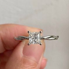 a person holding a ring with a diamond in it's center and two twisted bands around the band