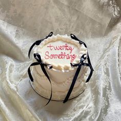 a white cake with black ribbon and writing on it sitting on a tablecloth covered surface