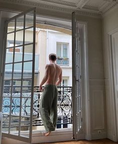 a shirtless man standing in front of an open door looking out at a balcony