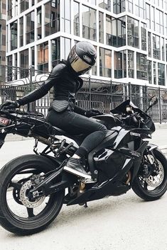 a person on a black motorcycle in front of a tall building with glass buildings behind it