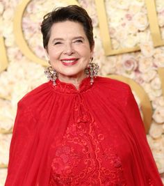 an older woman wearing a red dress and smiling at the camera with flowers in the background