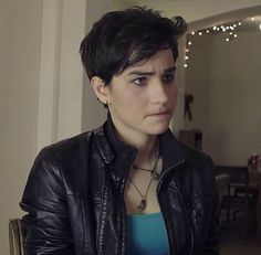 a woman with short hair wearing a black leather jacket and green top looking at the camera