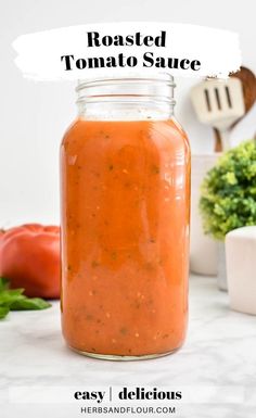 a jar filled with roasted tomato sauce on top of a white counter next to tomatoes