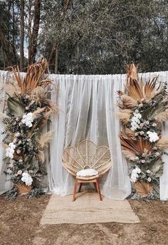 an outdoor ceremony setup with white drapes and flowers on the back wall, along with a wicker chair