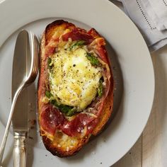 an open face sandwich on a white plate with a fork and knife next to it