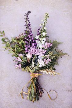 a bunch of purple and white flowers tied to a string on the ground with some green leaves