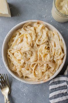 a white bowl filled with pasta and cheese next to a fork, knife and butter