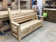 a woman standing next to a wooden bench in a shop with shelves and tools on the wall