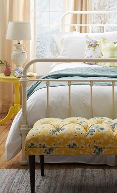 a white bed sitting next to a yellow table with a lamp on top of it