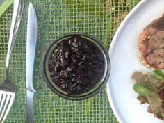 a white plate topped with meat and vegetables next to a bowl of black olives