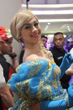 a woman in a blue dress is smiling at the camera while people look on from behind her