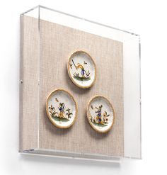 three small plates are on display in a glass case with linen backings and gold trim