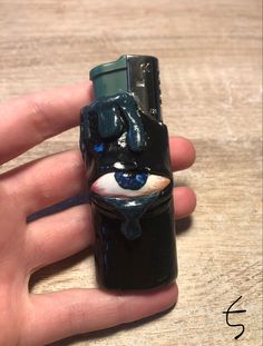 a hand holding a small black lighter with an evil face on it's side