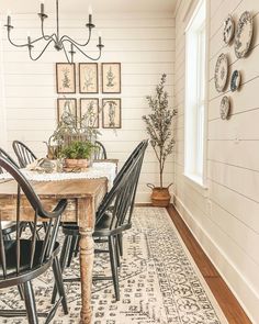 a dining room table with chairs and pictures on the wall above it, along with plants