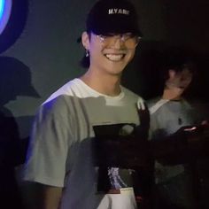 a young man wearing glasses and a baseball cap smiles at the camera while holding his cell phone