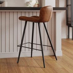 a brown leather bar stool sitting on top of a wooden floor next to a counter