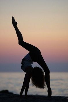 a woman doing a handstand on the beach at sunset with her arms in the air