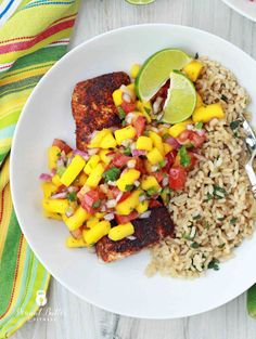 a white plate topped with rice and meat covered in mango salsa next to a fork