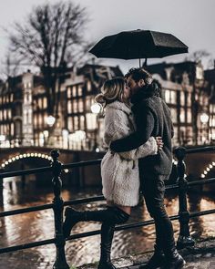 a man and woman kissing under an umbrella in the rain on a bridge over a river