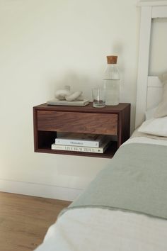 a nightstand with two books on it next to a bed