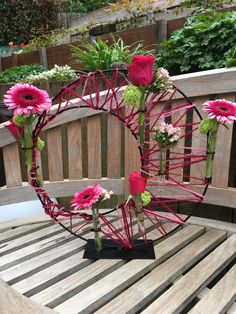 pink flowers are arranged in the center of a wire sculpture on top of a wooden bench