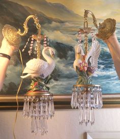 two chandeliers with swans on them are being held by someone's hand