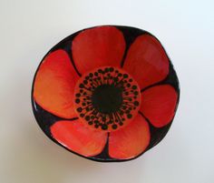 an orange and black flower is in a bowl on a white surface with the bottom half open