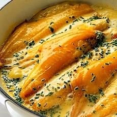 some fish is in a white dish with cheese and herbs on it's side