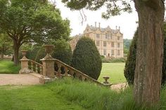 a large house with trees and bushes around it's perimeter in the middle of a lush green field