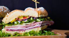 a large sandwich with meat, lettuce and tomato on it sitting in a wooden tray