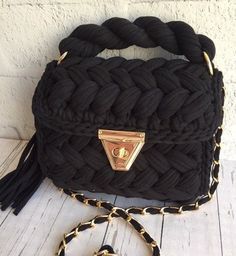 a black handbag with gold hardwares on the front and side, sitting on a white wooden floor