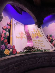 an open book on display in front of a wall with flowers and castle images painted on it