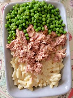 a white plate topped with pasta and meat next to green peas on top of a table