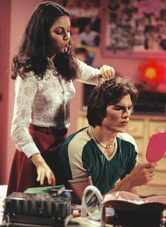 the young man is brushing his hair while the woman looks at her reflection in the mirror