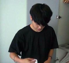 a young man standing in front of a toilet holding a white paper and looking at his cell phone