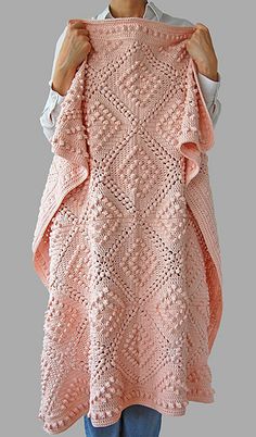 a woman holding up a pink knitted blanket