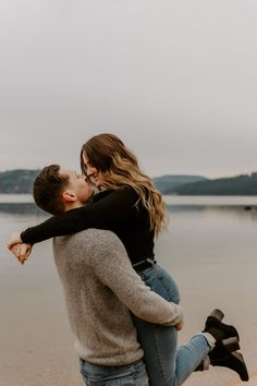 a man holding a woman on his back while she is kissing her forehead by the water